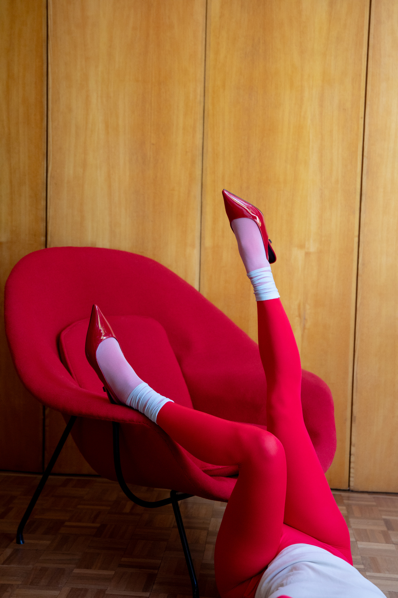 Legs in red tights and red heels stretched over a red armchair against a wood-panelled wall